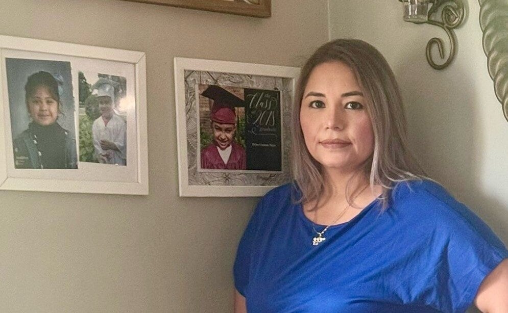 woman in blue dress standing next to framed photos of her children